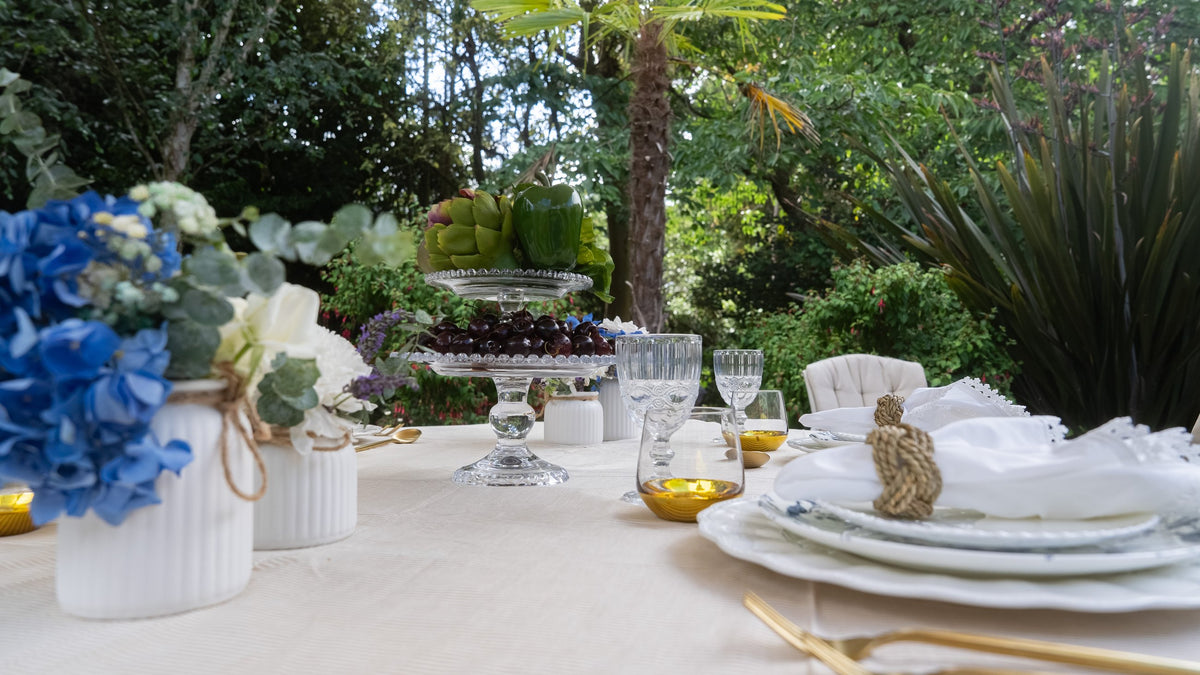 A garden table with tiered glass stands of cherries and vegetables, blue hydrangeas in white vases, amber tealights and rope-ringed napkins