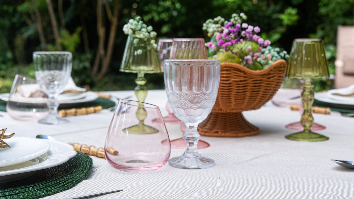 An outdoor table detail with mixed coloured glassware, a rattan basket of flowers and pears, and green woven placemats